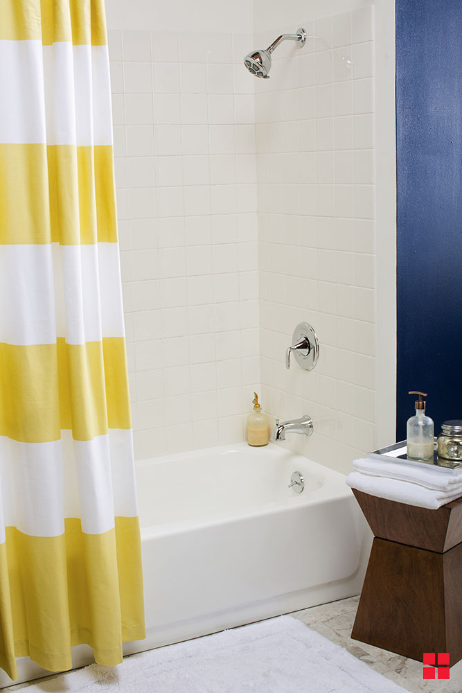A white bathtub with a white tile wall and yellow and white striped shower curtain.