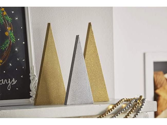 A silver wooden decorative tree on a mantel in front of two gold wooden decorative trees. 