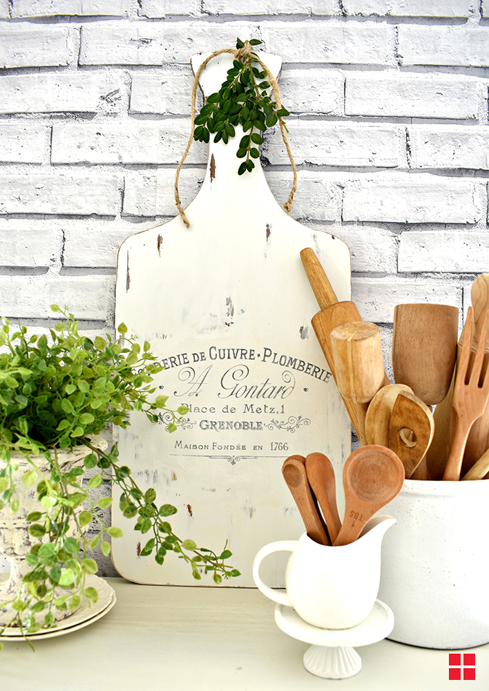Wooden cutting board painted white and decorated with words on a French label.