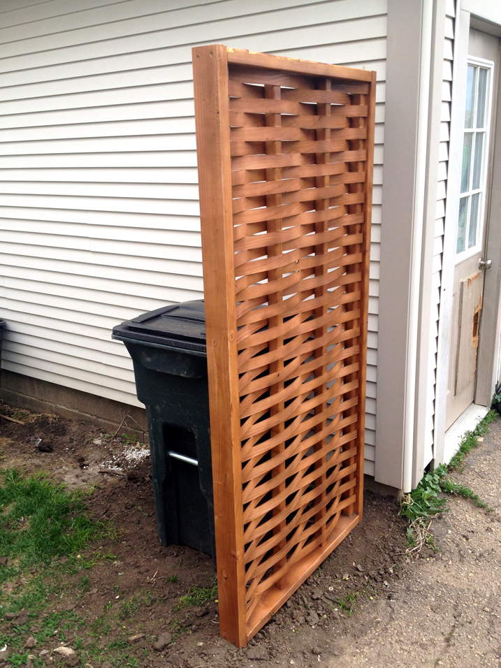 woven privacy screen hiding trash can next to a house