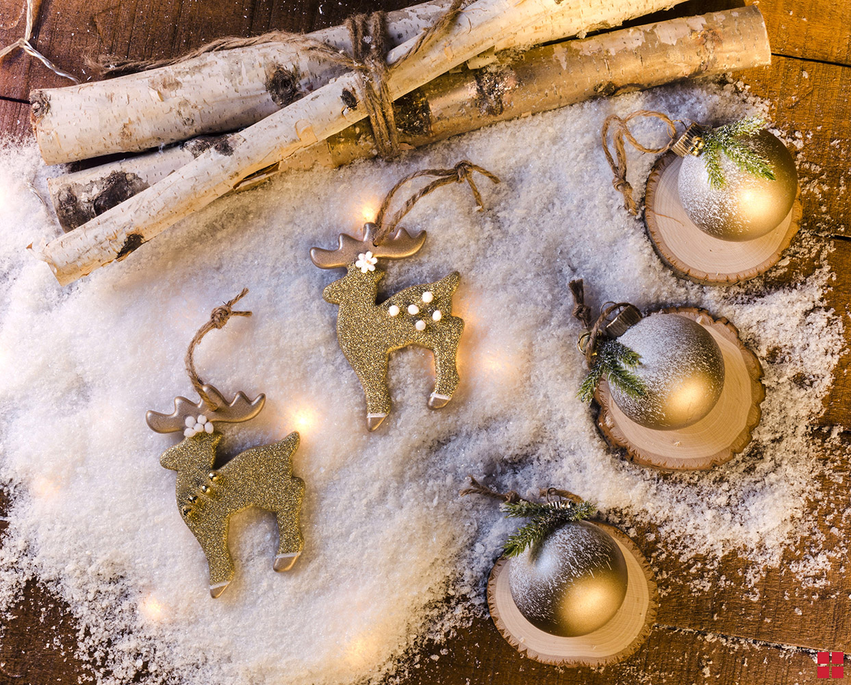 Glitter reindeer ornaments next to birch logs and gold ornaments.