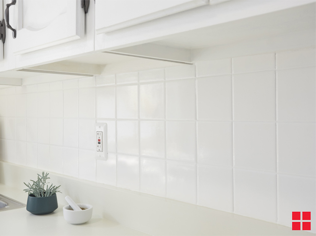 A white tile backsplash between an off-white countertop and white upper cabinets. 