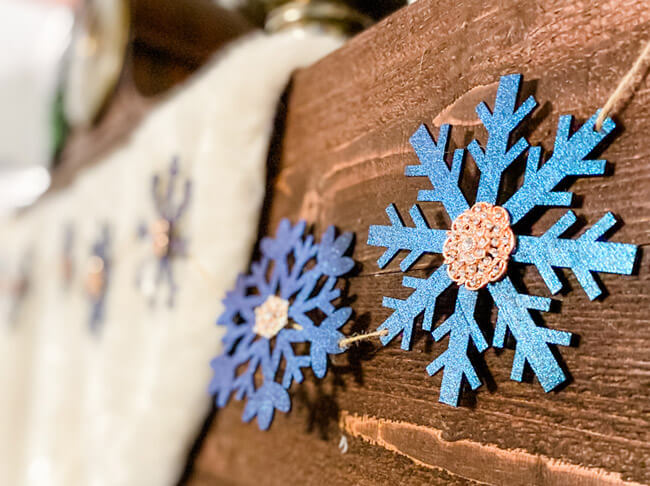 A string of decorative snowflakes in different shades of blue handing on a wooden mantle.