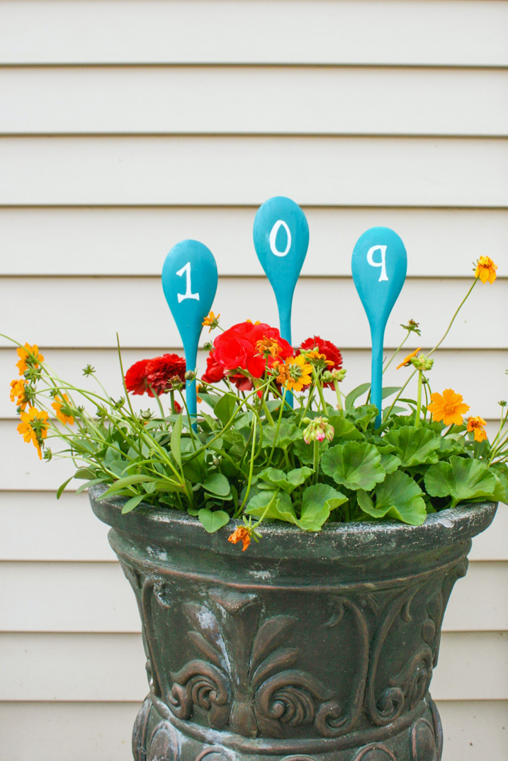 planter with flowers and spray painted wooden spoons sticking up with the house numbers on the spoons
