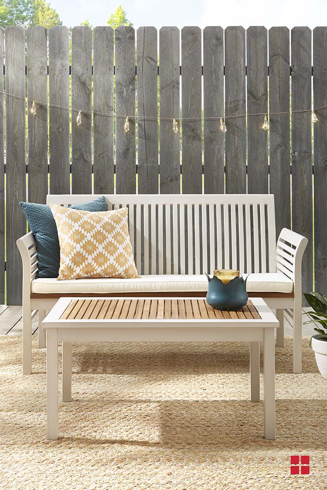 A light beige wooden bench and table on a deck in front of a wooden fence.