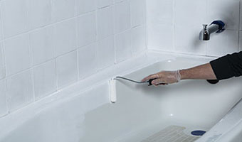 A gloved hand using a paint roller to apply white coating to a bathtub. 