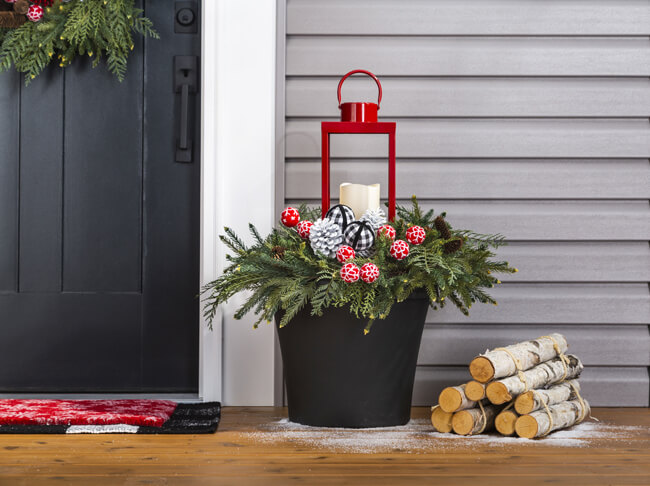 Black planter filled with greenery, pine cones and a red lantern.