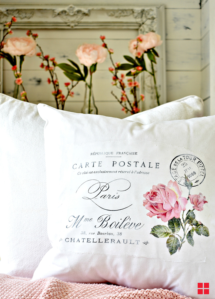 French words and a pink rose printed on a white pillow.