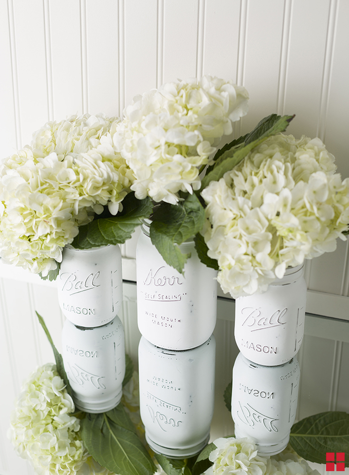 Three mason jars painted white and filled with hydrangeas.