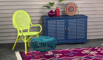 A florescent green chair, green metal table and a blue buffet with purple and coral vases and a multicolored basket displayed on top.
