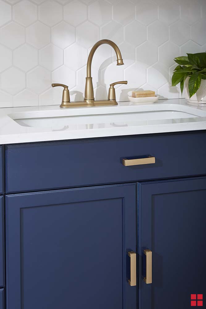 Navy blue cabinets with bronze handles under a sink with a bronze faucet. 