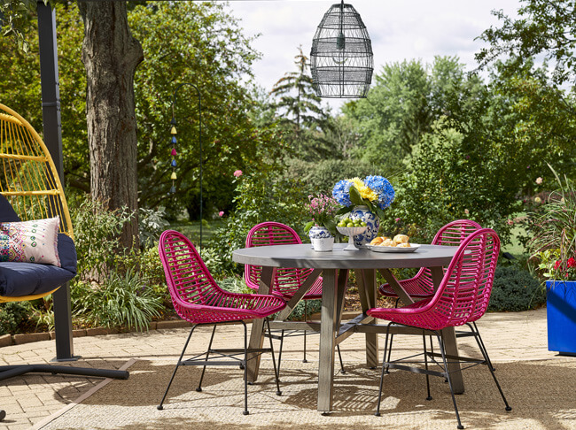 Outdoor patio with spray painted bright pink chairs, metallic blue painted planter and bright yellow painted hanging egg chair with a green pendent light above the table.  White planter and gold candlestick before painted beside a painted green planter and black candlestick