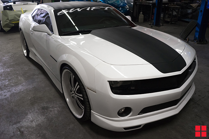 White car with a temporary black racing stripe painted on the center of the hood with Peel Coat spray paint.