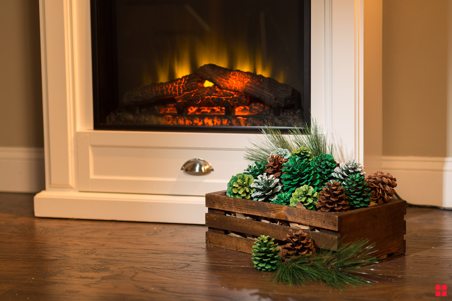 Glittery pine cones arranged in a wood crate near fireplace.