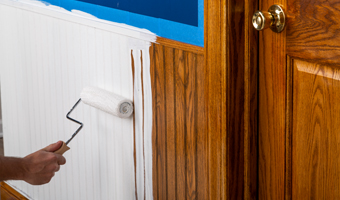 Using a paint roller to apply white primer over wood paneling.