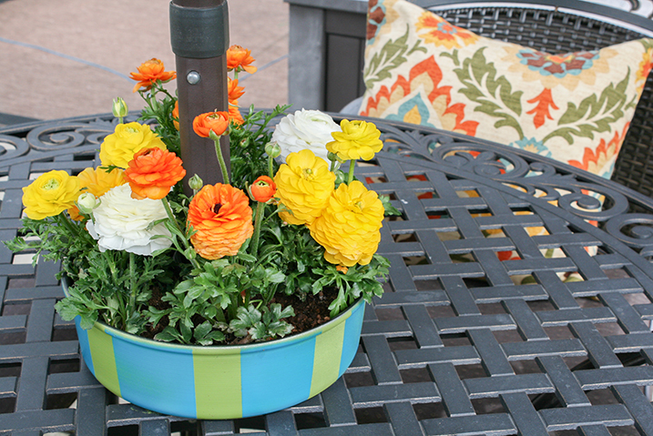 Flower planter painted green and blue sitting in the center of a patio table with the umbrella rod going through the middle 