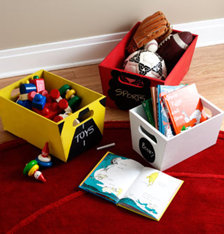 Three small bins with chalkboard labels on front. A yellow bin is labeled “Toys,” a red bin is labeled “Sports” and a white bin is labeled "Books.” 