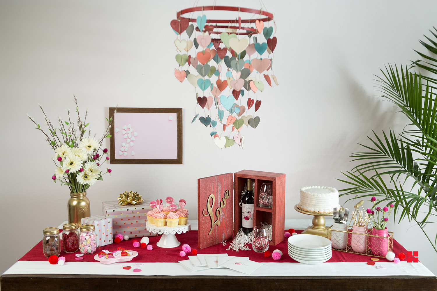 A wooden heart chandelier hanging over a table full of Valentine’s Day snacks and décor. 