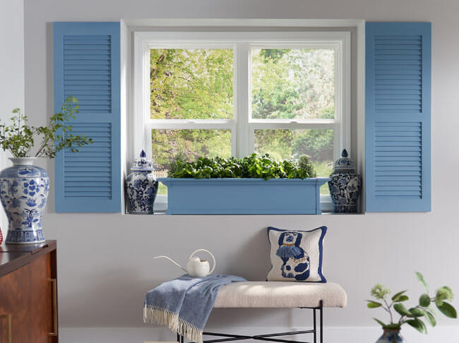 A window sill with a light blue planter on it and light blue indoor shutters on either side. 