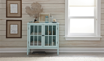 A light blue table with glass doors next to a window in a room with shiplap walls.