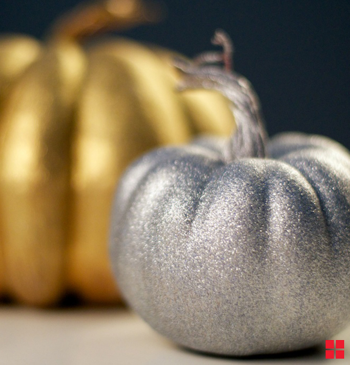 A glittery silver pumpkin in front of a gold glittery pumpkin. 