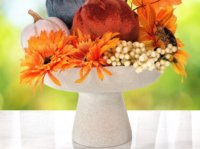 A white table centerpiece filled with artificial fall leaves, berries and pumpkins.