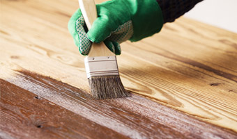 Close-up of a gloved hand staining a wood deck with a paint brush.