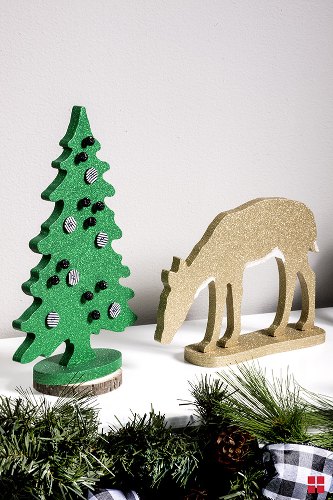 Green glittery wood Christmas tree with buttons glued on it next to a gold glittery wooden reindeer. 