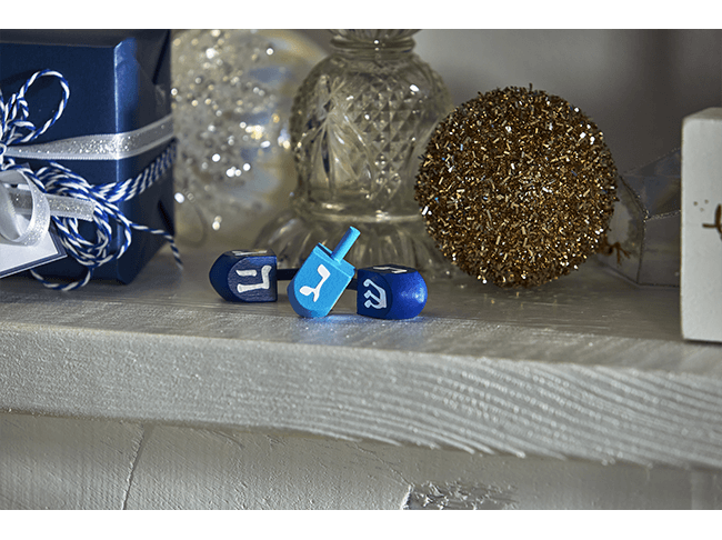 Two dark blue dreidels and one lighter blue dreidel arranged on a mantel. 