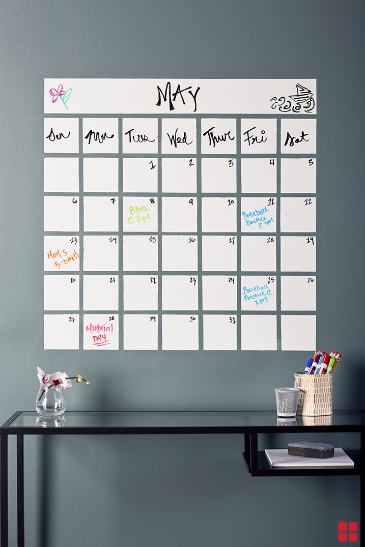 A dry erase calendar painted on a wall above a table.