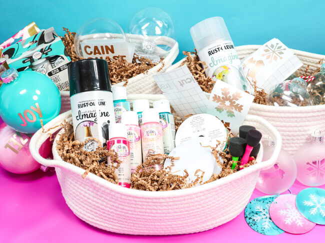 Painted ornaments on a table next to three white baskets containing Rust-Oleum and Testors paint products. 